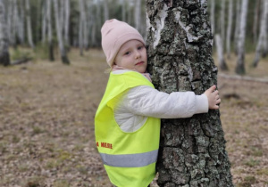 Dziewczynka przytula się do drzewa.
