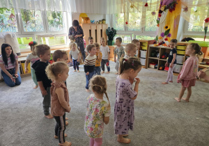 Dzieci stoją na dywanie, bawią się w zabawę ruchową.