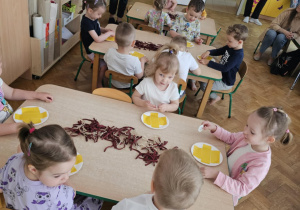 Dzieci wykonują pracę plastyczną przy stolikach.