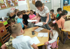 Pani Ania rozdaje dzieciom siedzącym przy stolikach kartony, które zamienione zostaną w okładki książek.