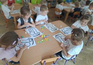Dzieci siedzą przy stoliku i wyklejają warszawską syrenkę.