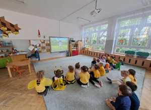 Dzieci siedzą na dywanie i oglądają film edukacyjny o Pszczołach.