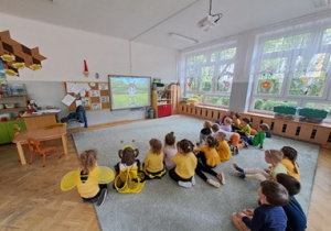 Dzieci siedzą na dywanie i oglądają film edukacyjny o Pszczołach.