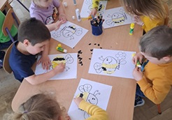 Dzieci siedzą przy stolikach i robią pracę plastyczną.