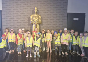 Grupowe zdjęcie dzieci przed statuetką Oscara.