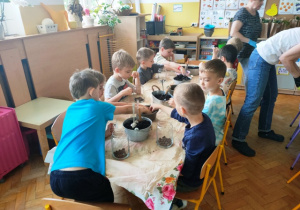 Dzieci umieszczają kolejno w szklanym naczyniu keramzyt, perlit oraz ziemię.