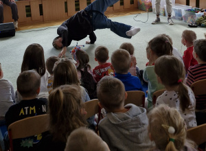 Dzieci siedzą na widowni i oglądają pokaz tańca hiphopowego.