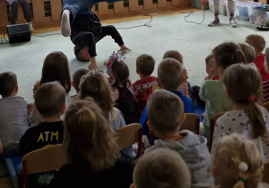 Dzieci siedzą na widowni i oglądają pokaz tańca hiphopowego.