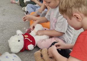 Dzieci udzielają pierwszej pomocy swoim ukochanym maskotkom - naklejają plastry.