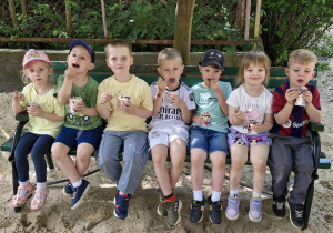 Dzieci siedzą na ławce i zajadają pyszne lody.