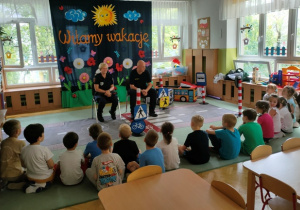 Dzieci siedzą w dużym półkolu, odpowiadają na pytania kierowane do nich przez przedstawicieli służb mundurowych.