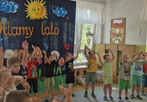Dzieci tańczą do wesołej piosenki i machają rękoma uniesionymi w górę.