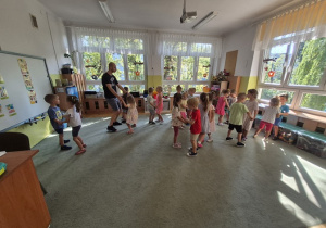 Dzieci stoją w parach na dywanie trzymają się za ręce i uczą się kroku samby.