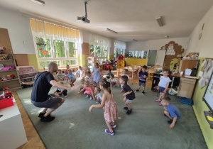 Dzieci stoją w rozsypce na dywanie i rozgrzewają się do zajęć.