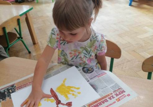 Dziewczynka stempluje na kartonie dłonią prawe skrzydło motyla.