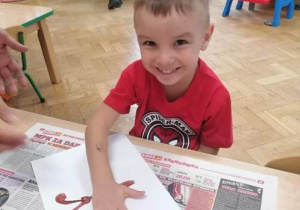 Chłopiec na kartonie odbija pomalowaną na żółto dłoń tworząc lewe skrzydło motyla.
