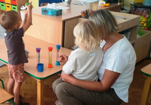 Dzieci wraz z ciocią przy stoliku bawią się tubami sensorycznymi.