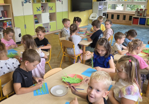 Dzieci siedzą przy stolikach i wykonują pierwszą pracę plastyczną.