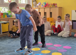 Dwóch chłopców skacze po kolorowych kropkach naklejonych na dywanie.