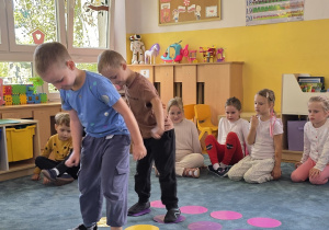 Chłopcy skaczą po kolorowych kropkach przyklejonych na dywanie zgodnie z rytmem piosenki.