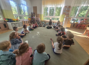 Dzieci siedzą na dywanie i słuchają o programowaniu robota.