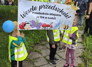 Dzieci trzymają transparent z napisem: Wesołe Przedszkole.