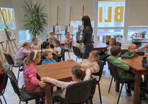 Pani bibliotekarka pokazuje dzieciom ilustracje z wiersza.