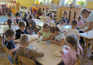 Dzieci siedzą przy stolikach i kroją owoce do sałatki.