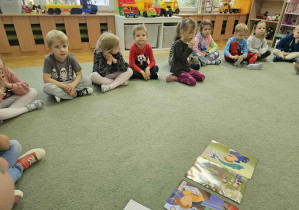 Dzieci siedzą na dywanie i słuchają opowiadania.