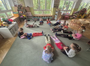 Dzieci leżą na dywanie i wykonują masaż relaksacyjny twarzy.