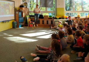 Dzieci oglądają film edukacyjny, z uwagą słuchają wypowiedzi prowadzącej.