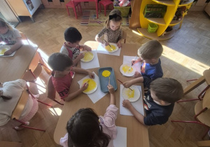 Dzieci siedzą przy stolikach i tworzą swoje emotki.