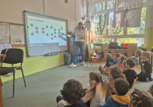 Dzieci siedzą na dywanie oglądają prezentację multimedialną.