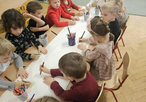 Dzieci siedzą przy stolikach i wykonują pracę.