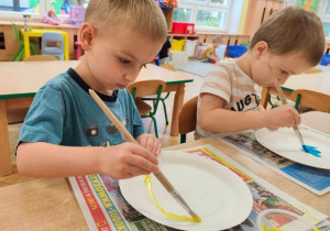 Chłopcy malują farbami talerzyk papierowy , który będzie bazą do stworzonej przez nich emotki.