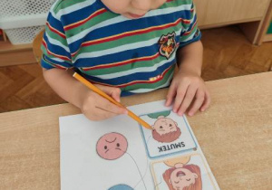 Chłopiec łączy w pary : emotkę wyrażającą nastrój dziecka na obrazku.