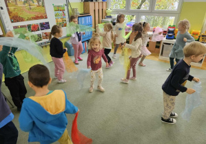 Dzieci tańczą z kolorowymi chustami na dywanie do muzyki klasycznej.