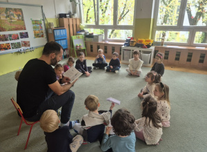 Dzieci siedzą na dywanie i słuchają opowiadania.