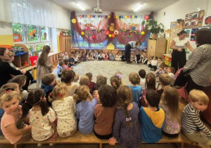 Na chwilę przed występem - dzieci młodsze siedzą w półkolu na dywanie, goście zajęli miejsca w drugiej części sali.