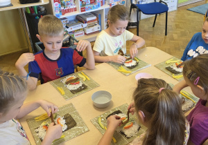 Dzieci wybierają kolejne składniki sushi i układają je na ryżu.