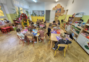 Dzieci siedzą przy stolikach i wykonują prace plastyczną.