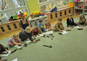 Dzieci starają się ułożyć z kasztanów cyfrę 1.