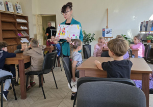 Dzieci siedzą przy stolikach i słuchają książki Katarzyny Puchalskiej pt. "Prezenty od złości".