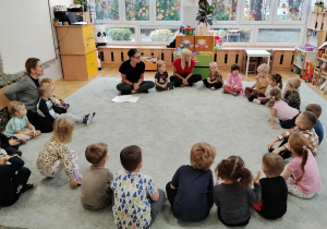 Dzieci siedzą w kole i uważnie słuchają.