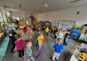 Dzieci tańczą na dywanie z kolorowymi chustami.