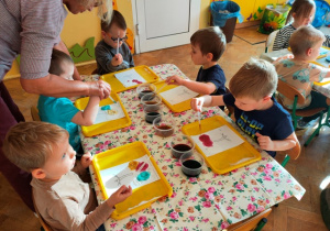 Dzieci za pomocą pipety przenoszą kolorowy płyn na koronę drzewa pokrytego sodą oczyszczoną.
