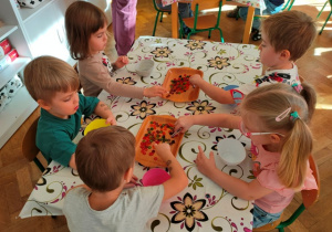 Dzieci za pomocą pęset przenoszą kolorowe koraliki do swoich miseczek.