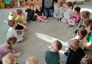 Dzieci siedząc w kole śpiewają piosenki.