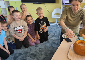 Dzieci obserwują jak Pani Kasia wlewa ocet do środka wydrążonej dyni wypełnionej sodą oczyszczoną.