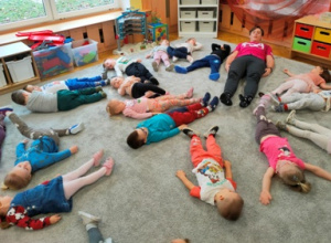 Dzieci leżą na dywanie na plecach- naśladują ruchy nóg w stylu grzbietowym.